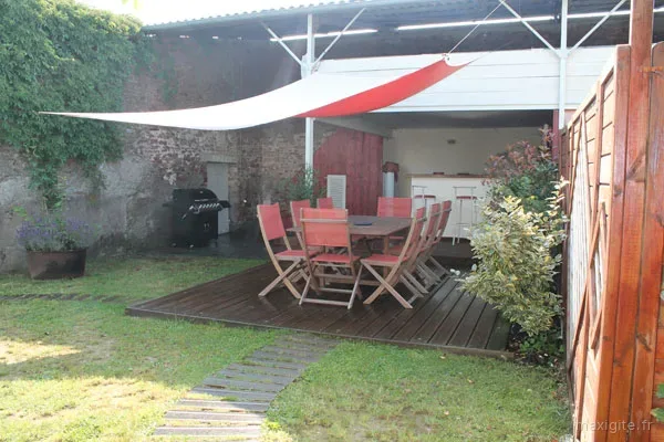 Terrasse en bois avec grande table et chaises rouges sous voile d'ombrage