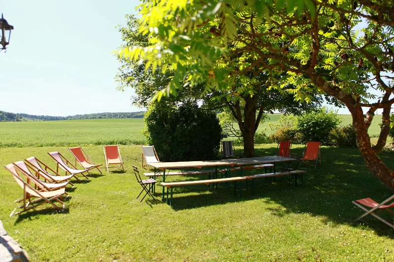 Coin détente extérieur avec chaises longues colorées et grande table sous les arbres