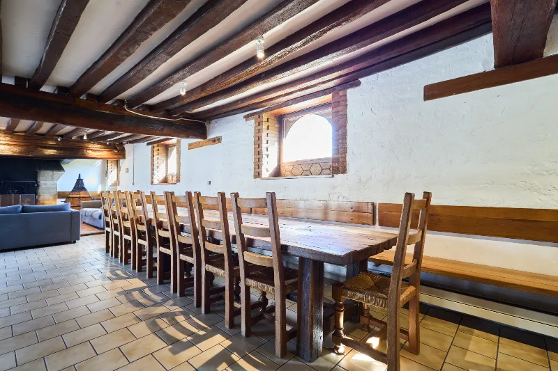 Longue table en bois massif dressée avec un bouquet de blé sous les poutres apparentes du séjour