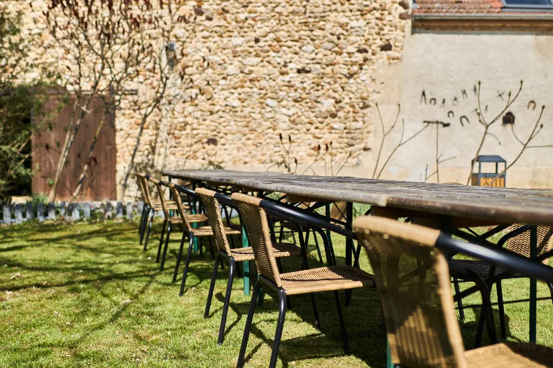 Longue tablée dressée dans le jardin devant le mur en pierre pour les repas de groupe