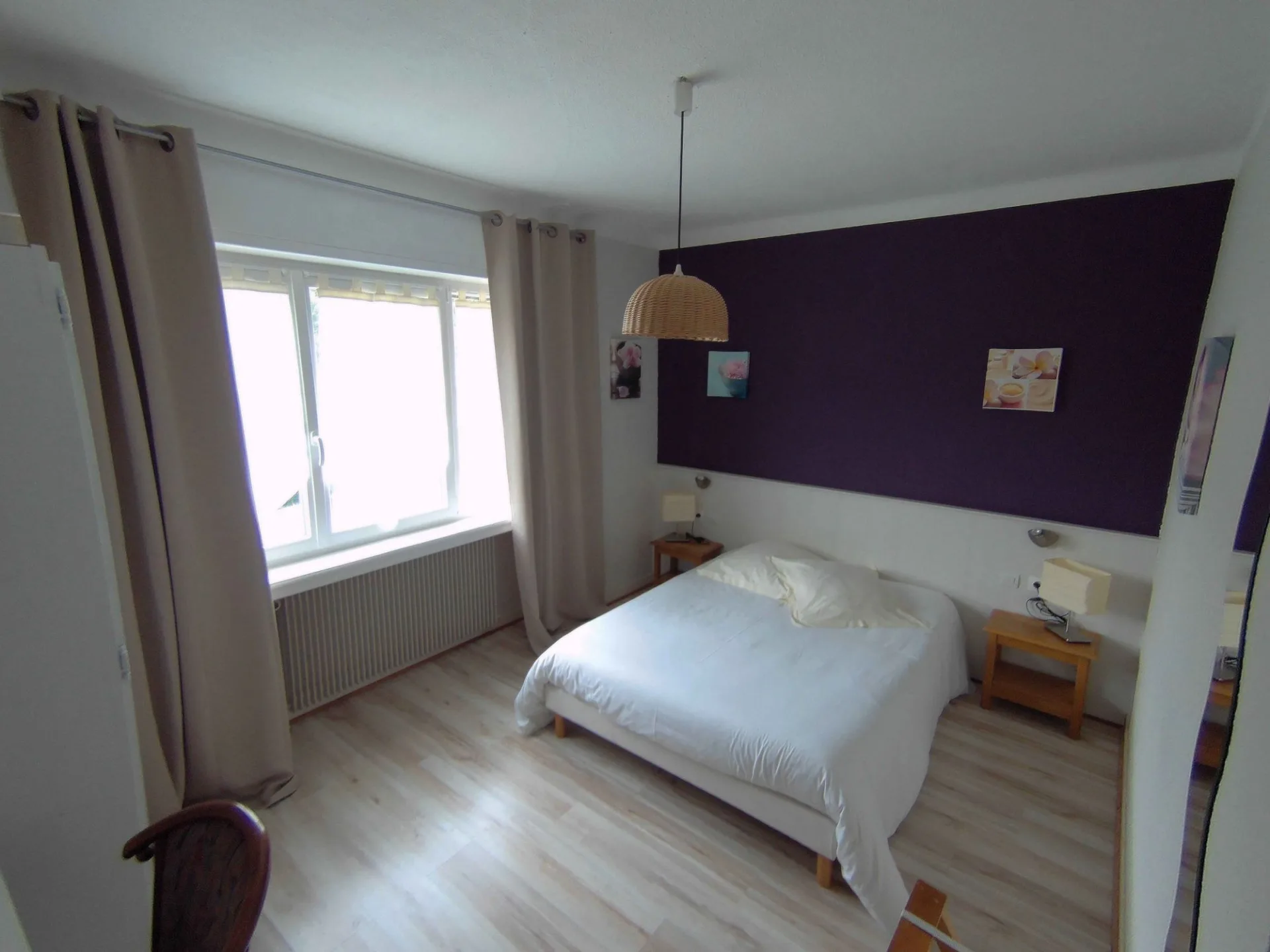 Chambre double avec tête de lit violette, literie blanche et grande fenêtre lumineuse