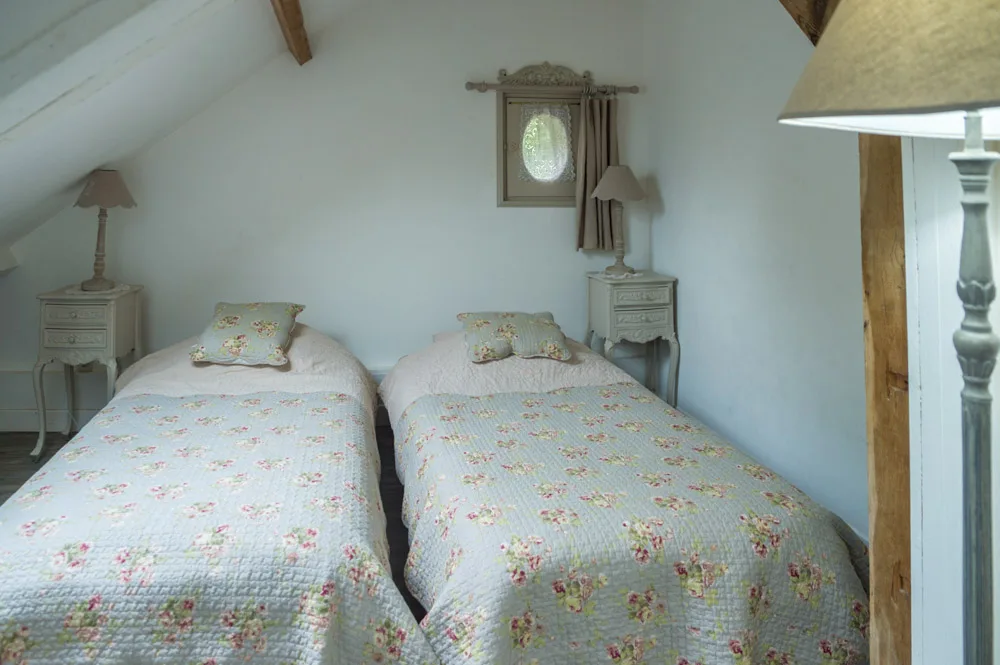 Chambre lumineuse avec deux lits simples et tissus fleuris sous les combles