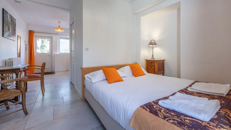 Chambre avec grand lit, coussins orange et petit salon attenant