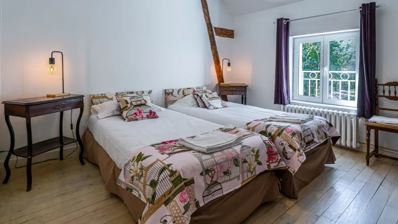 Chambre avec deux lits jumeaux, poutre apparente et balcon donnant sur les arbres