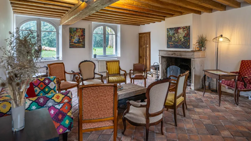 Salon avec poutres apparentes, cheminée en pierre et fauteuils colorés autour d'une table basse
