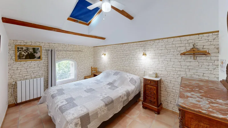 Chambre en pierres apparentes avec lit double, commode ancienne et grande table en bois