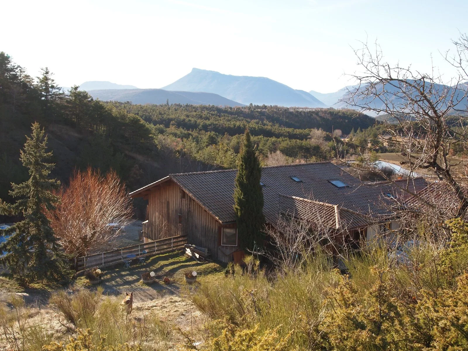 Vue d'ensemble du gîte en bois sous son toit de tuiles, entouré de montagnes du Haut-Buëch