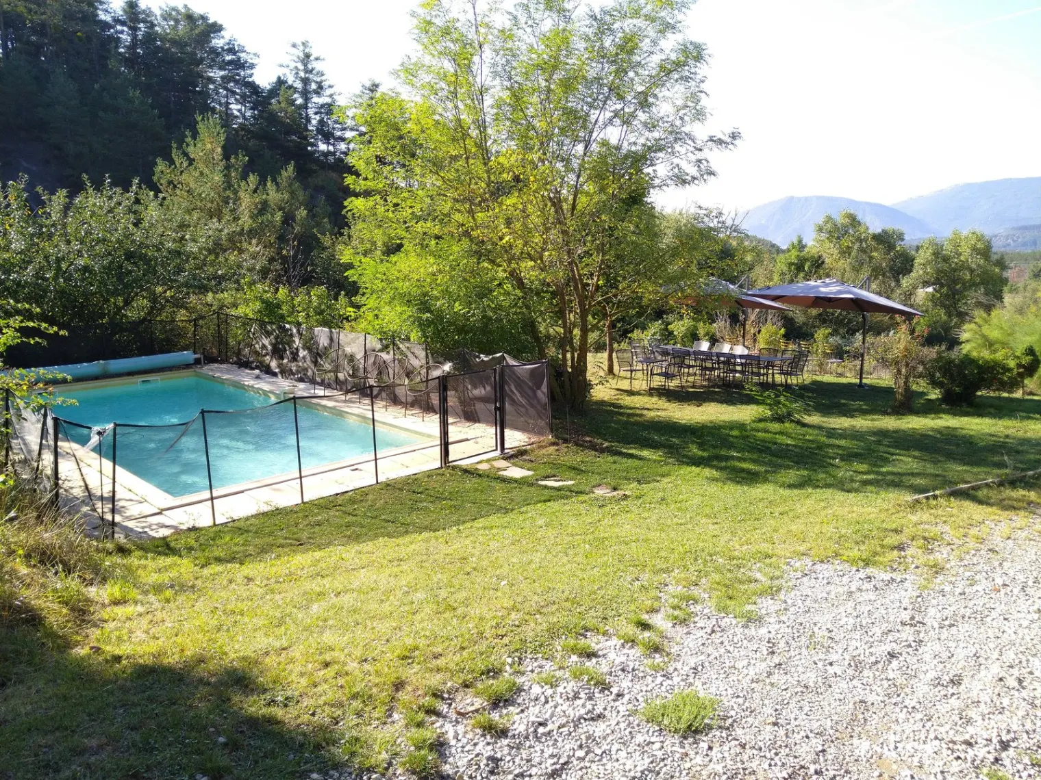Piscine extérieure sécurisée entourée de verdure avec grande table et parasols à proximité