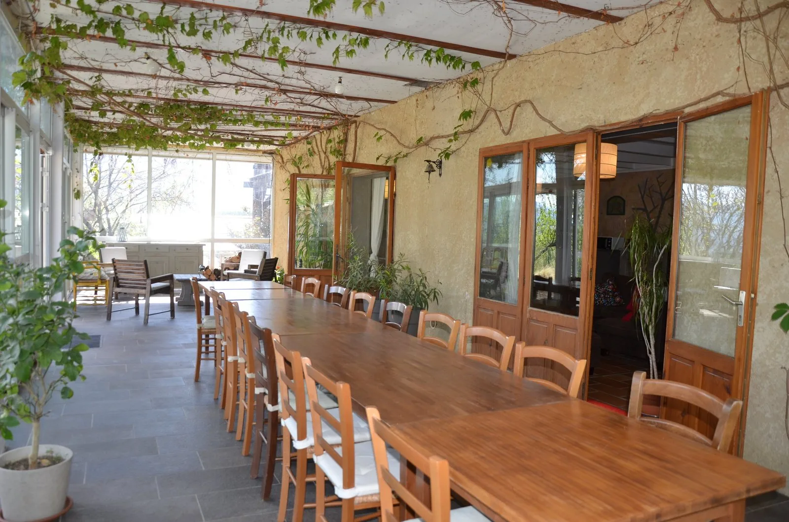 Longue table en bois dressée pour un grand groupe dans la véranda ouverte sur le jardin