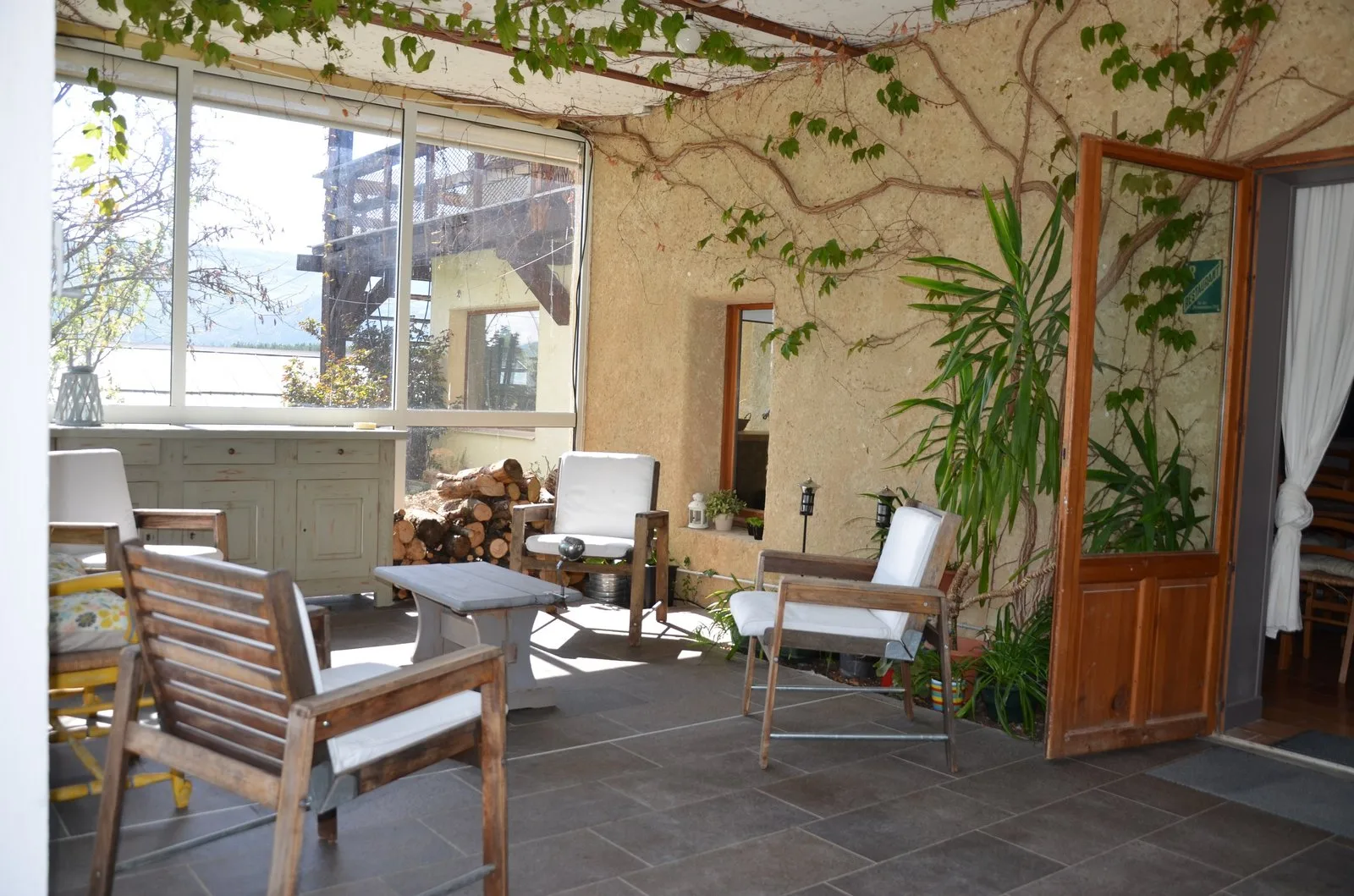 Coin salon de la véranda avec fauteuils en bois et vue sur la campagne environnante
