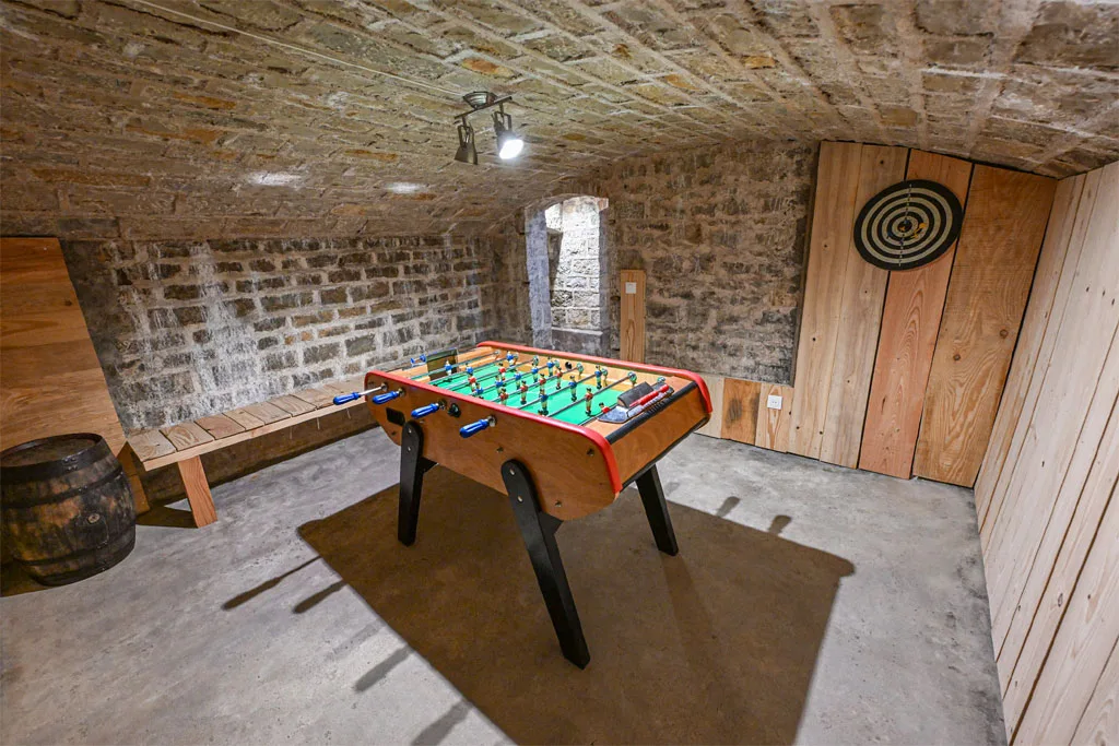 Cave de jeux voûtée en pierre avec baby-foot et jeu de fléchettes