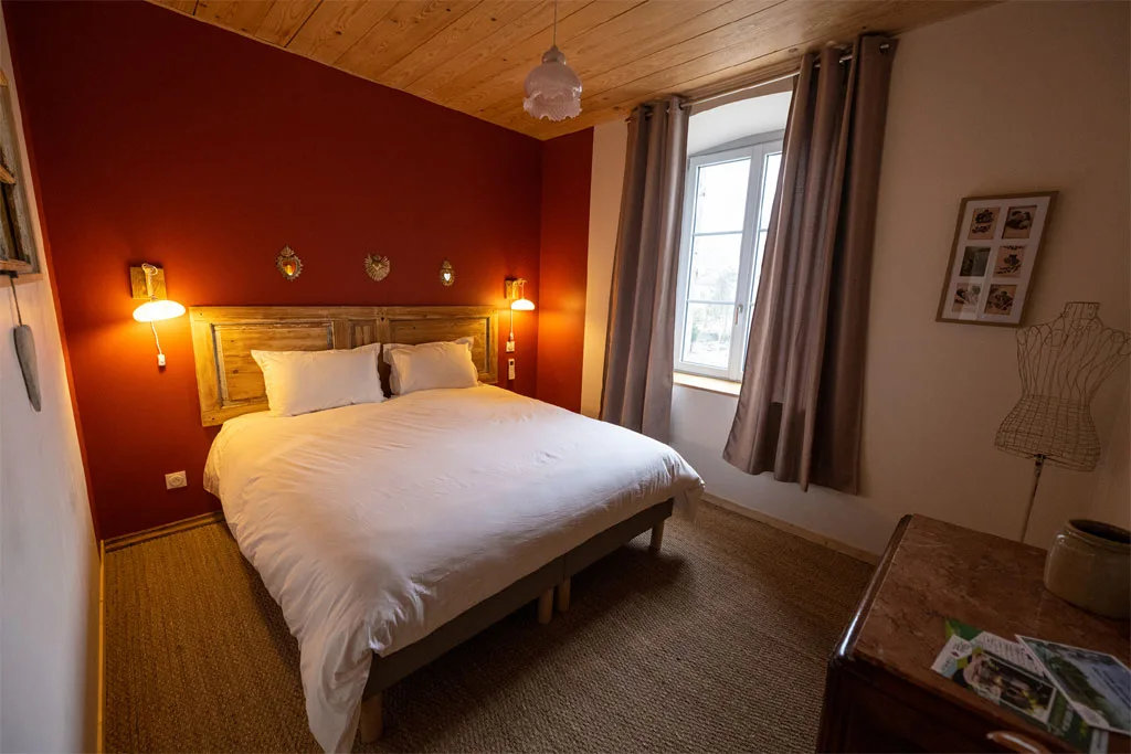 Chambre double avec mur bordeaux et tête de lit en bois ancien
