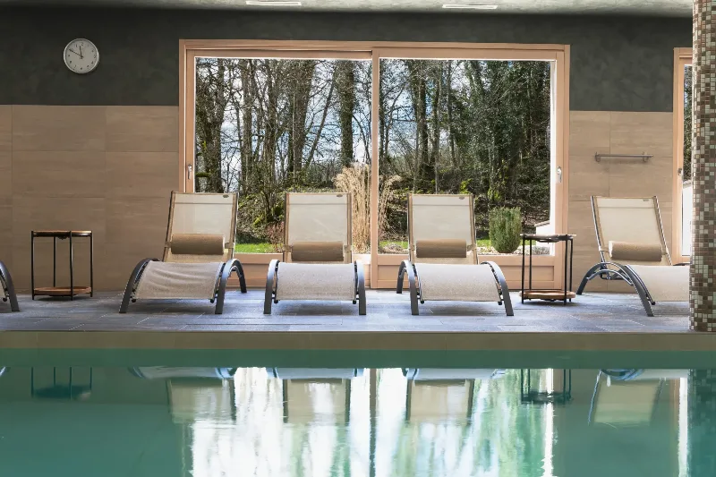 Piscine intérieure chauffée avec transats et grandes baies vitrées sur la nature