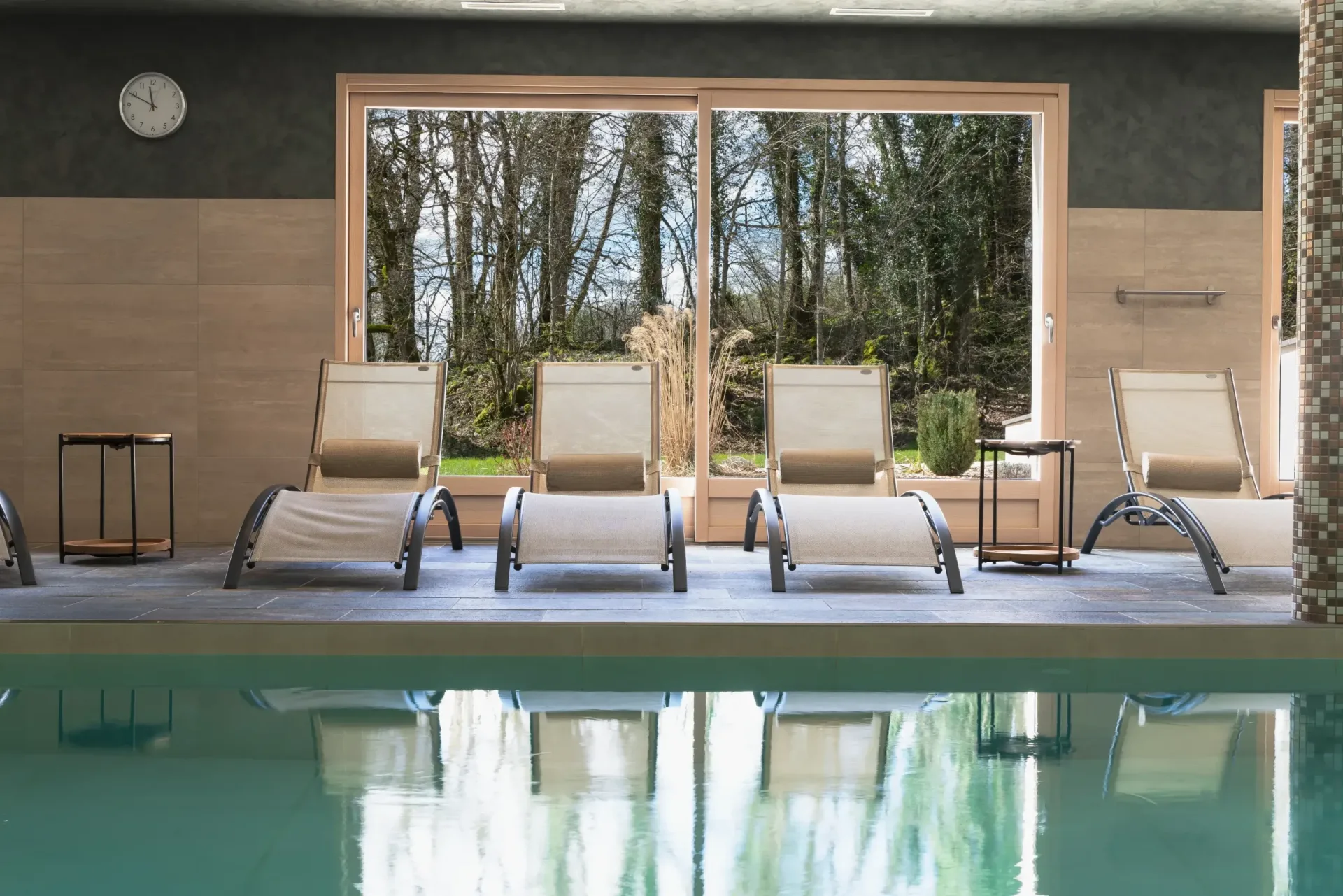 Piscine intérieure chauffée avec transats et grandes baies vitrées sur la nature