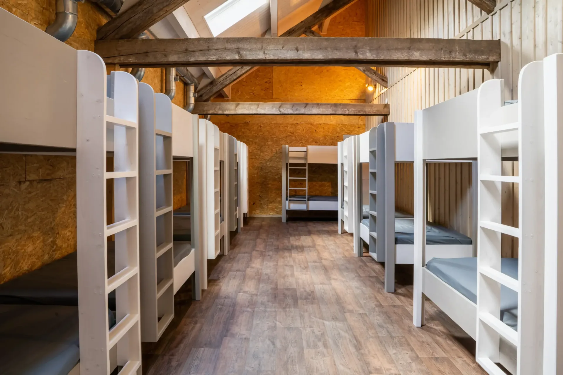 Dortoir avec lits superposés en bois blanc pour 22 couchages sous charpente apparente