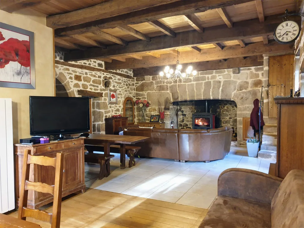 Salon avec poêle à bois, canapés en cuir et poutres apparentes sous charpente ancienne