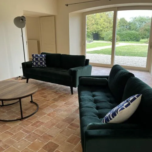 Salon avec canapés verts et grande baie vitrée ouvrant sur le jardin