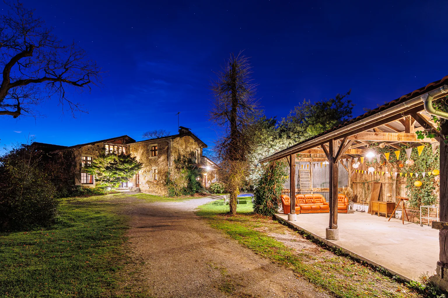 Gîte de groupe Domaine Lacampagne à Ossages — Façade en pierre du domaine de nuit avec cour arborée éclairée, capacité 20 personnes