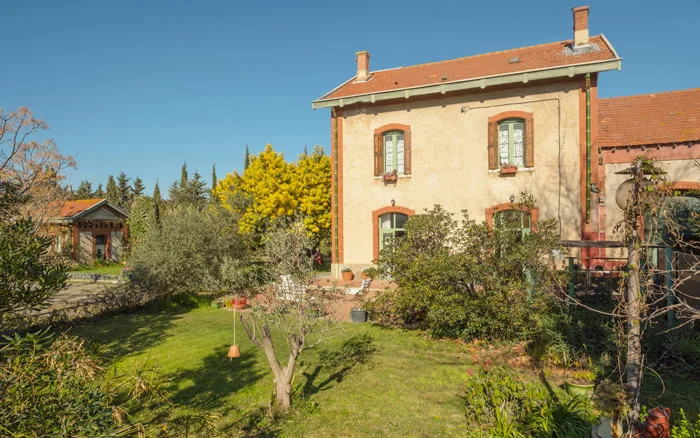 Façade et terrasse avec salon de jardin en fer forgé sous un olivier