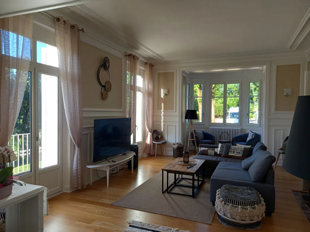 Grand salon lumineux avec canapé, cheminée et baies vitrées