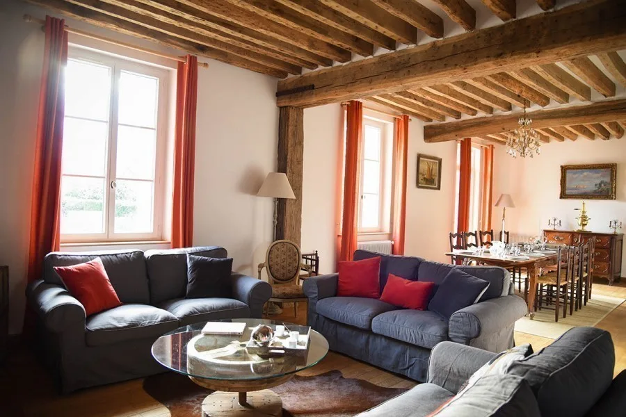 Second salon lumineux avec canapés et fenêtres à rideaux orangés