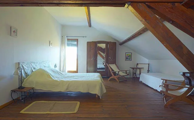 Chambre mansardée sous charpente en bois avec deux lits et chaise longue