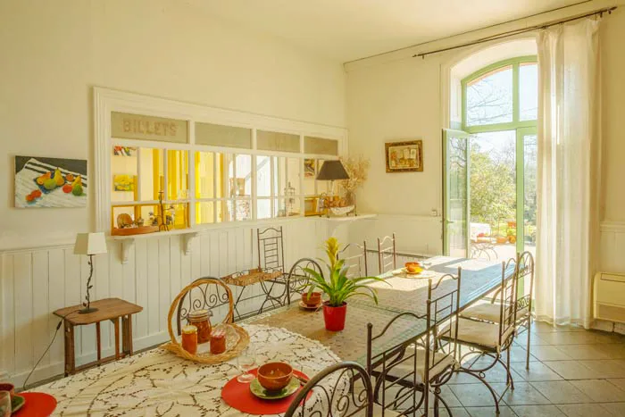 Salle à vivre dans l'ancien guichet, table en bois et grande verrière BILLETS d'origine
