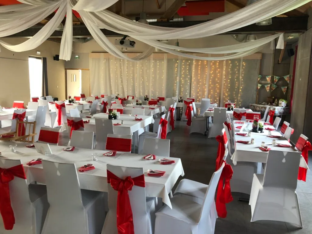 Grande salle de réception dressée pour un mariage avec tables et nappage blanc
