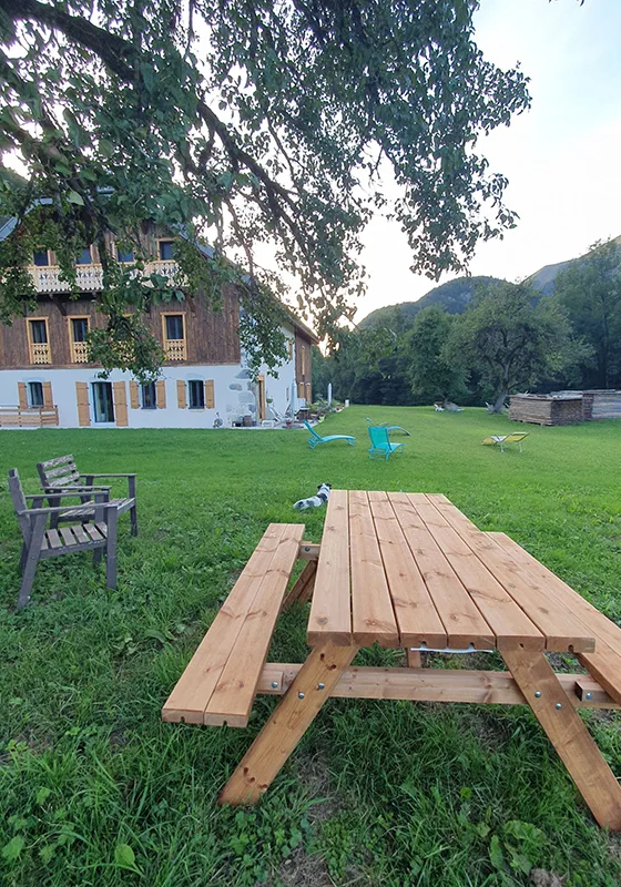 Jardin arboré avec table de pique-nique en bois face à la ferme et aux montagnes
