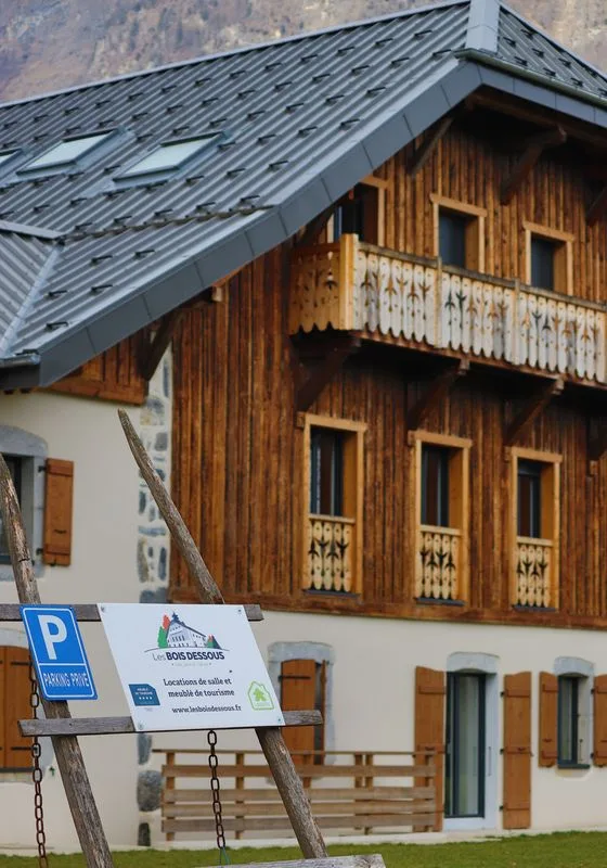 Gîte de groupe Les Bois Dessous à Châtillon-sur-Cluses — Façade en bois et pierre de la ferme savoyarde avec panneau Les Bois Dessous et parking, capacité 15 personnes