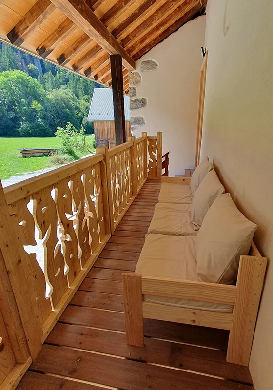 Banquette en bois sur la terrasse couverte avec vue sur la prairie et un chalet voisin