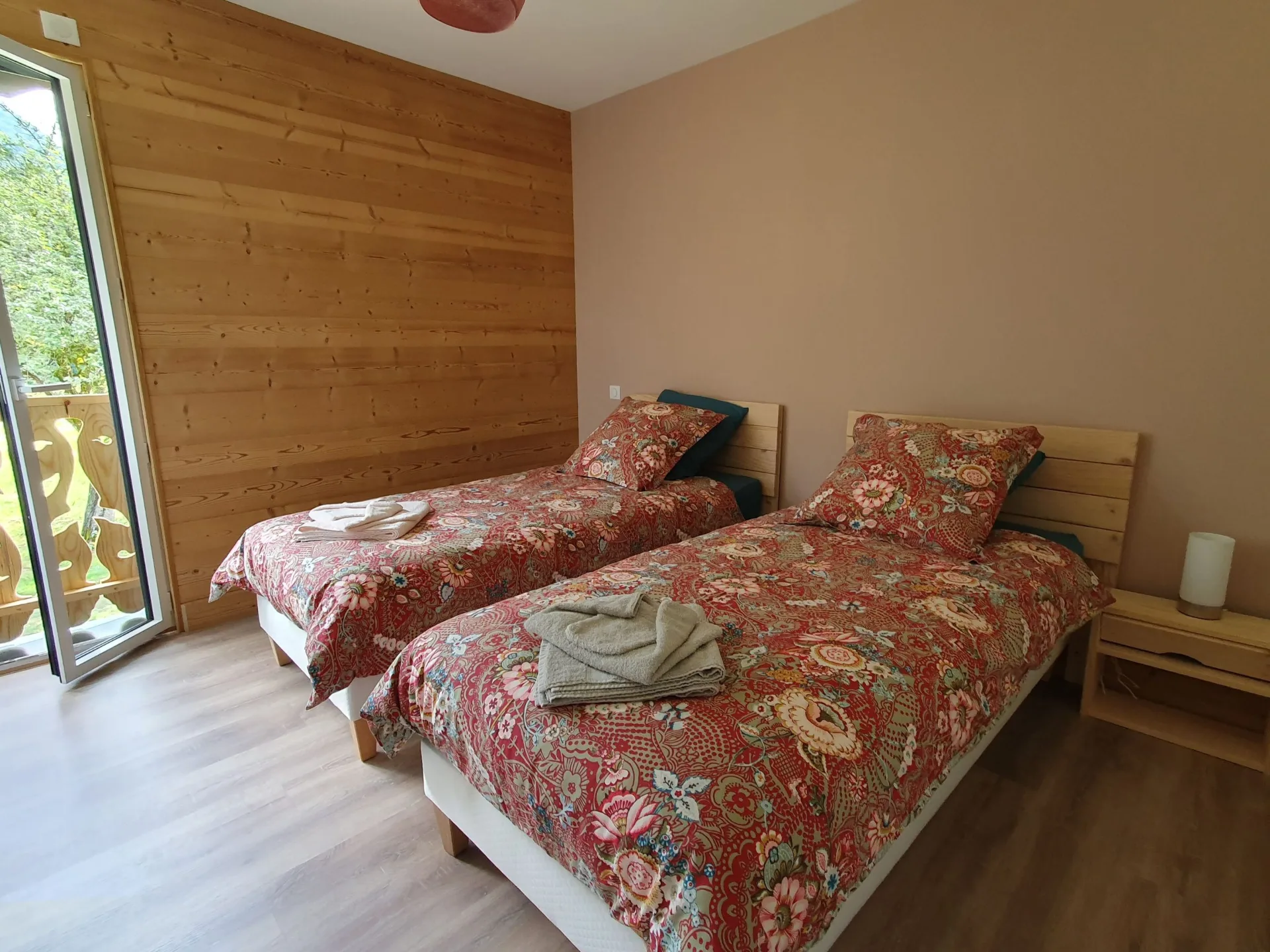 Chambre avec deux lits jumeaux à parure fleurie et accès balcon donnant sur la prairie