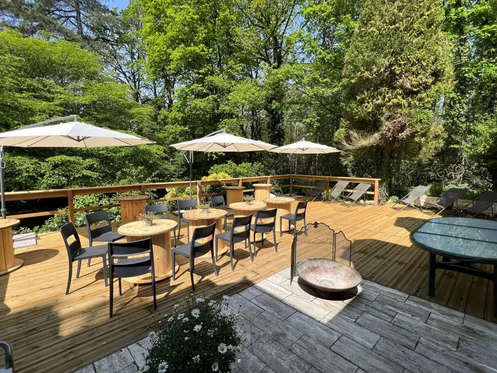 Terrasse en bois avec tables rondes, chaises et parasols au milieu des arbres