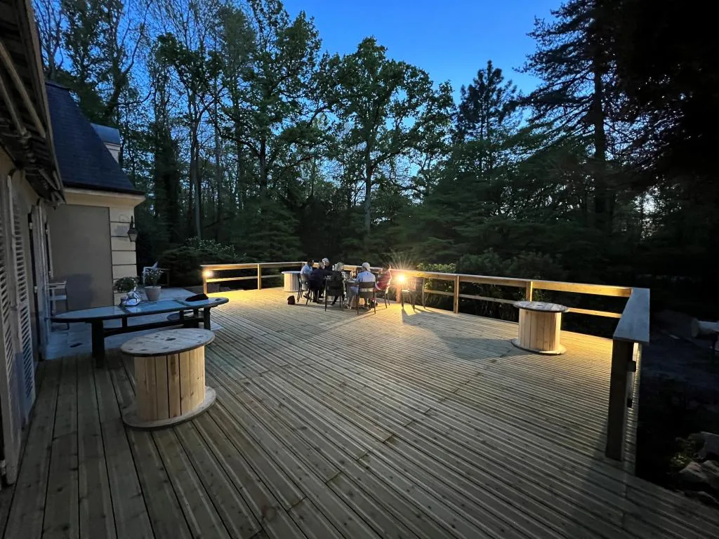 Terrasse extérieure éclairée en soirée avec groupe attablé sous les arbres