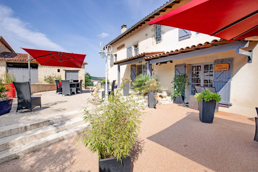 Façade en pierre du domaine avec toit en tuiles, terrasse fleurie et parasol rouge