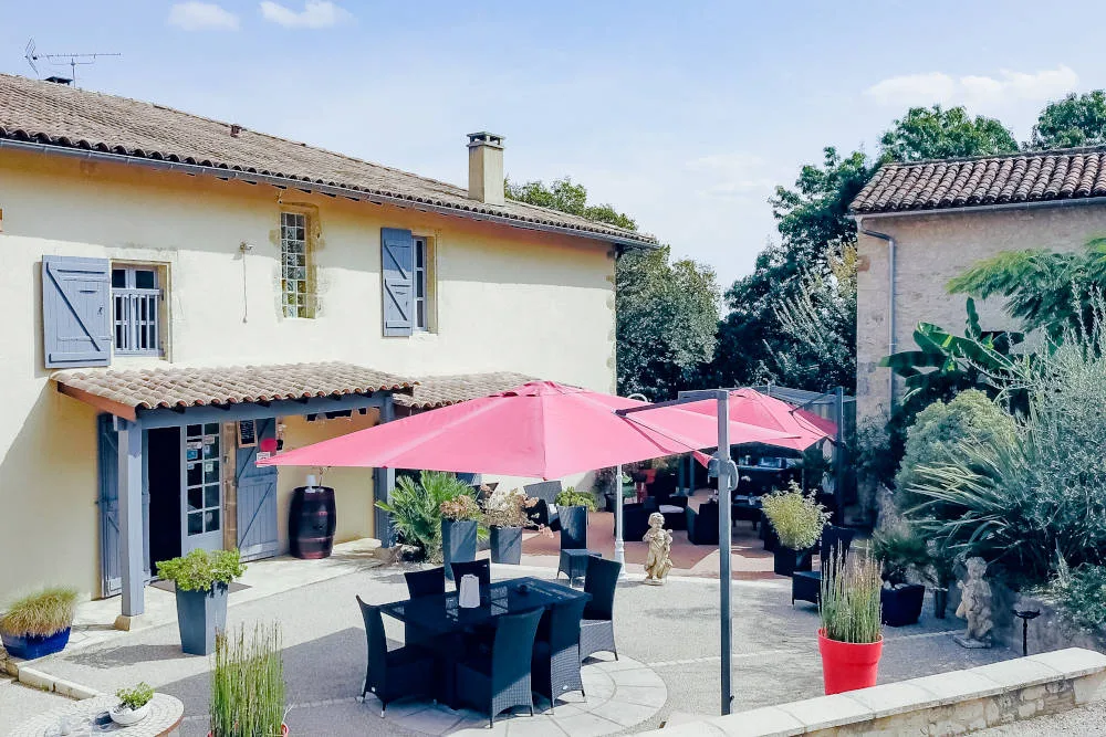 Terrasse extérieure ombragée avec parasol rose et salon de jardin devant la façade
