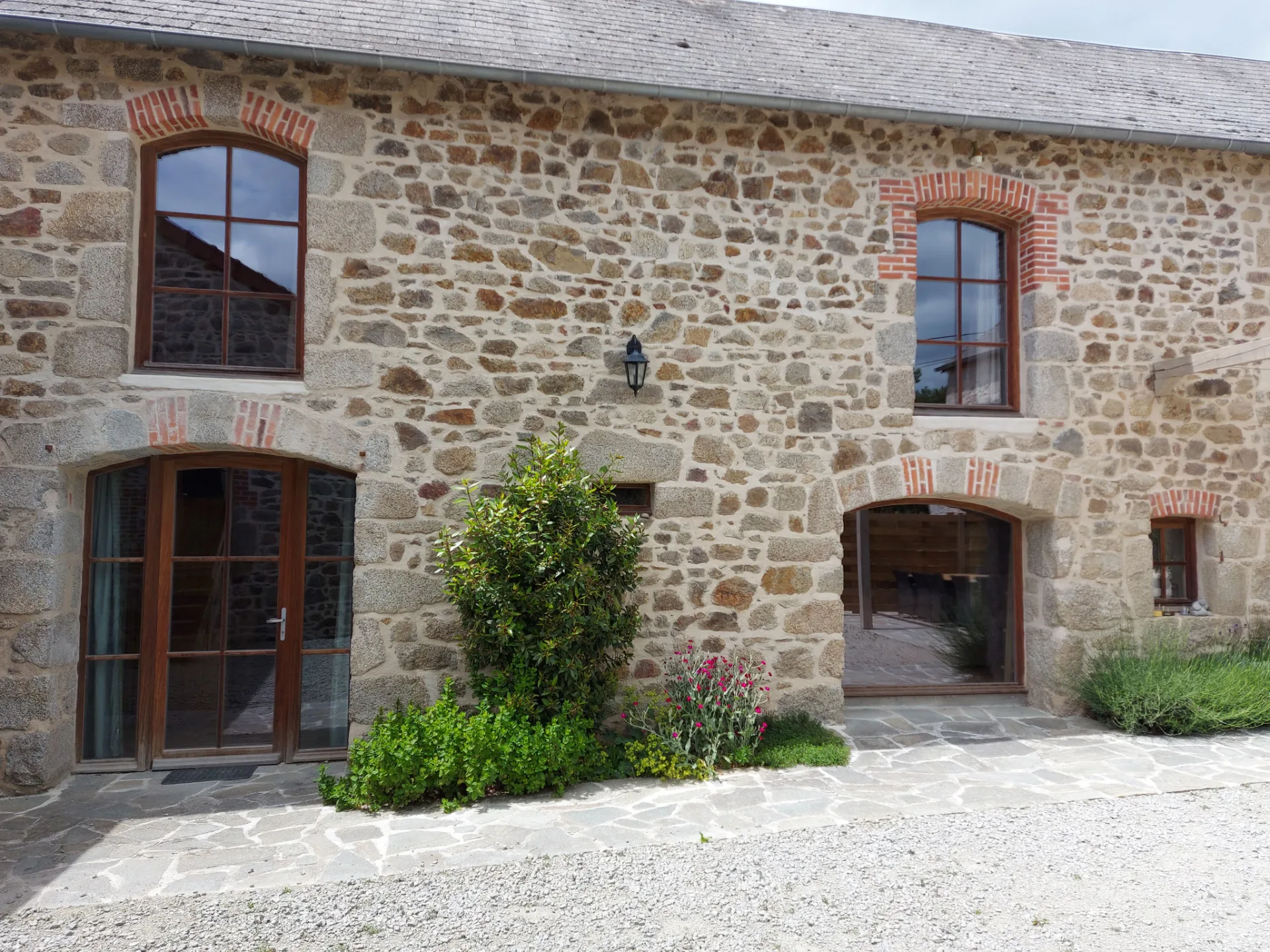 Gîte de groupe L'Élémentaire à Charensat — Façade en pierre du gîte avec fenêtres à encadrement de brique et terrasse en pierre, capacité 25 personnes