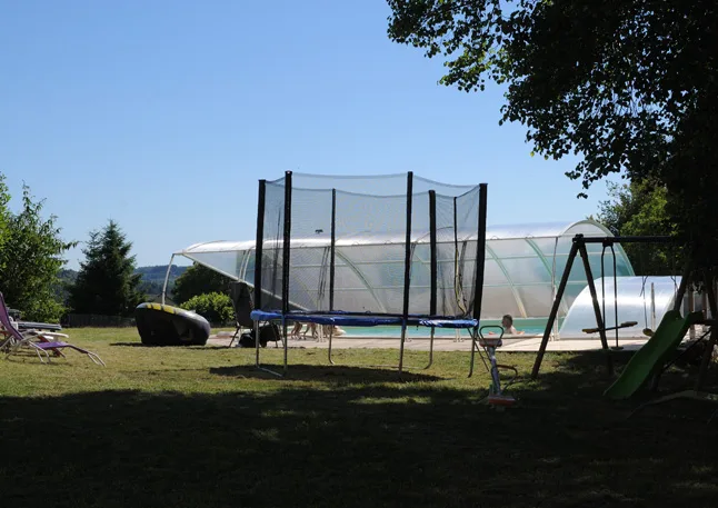 Piscine balnéo couverte sous tunnel, avec trampoline, balançoire et toboggan dans le jardin