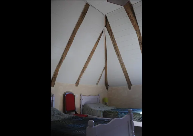 Chambre mansardée avec deux lits simples sous la charpente en bois