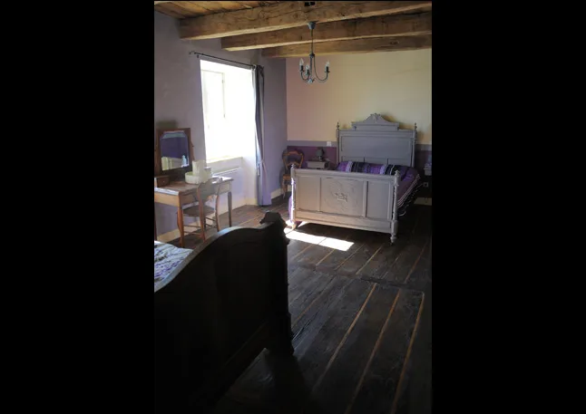 Chambre avec lit ancien en bois et second lit à l'ambiance mauve, sous poutres apparentes