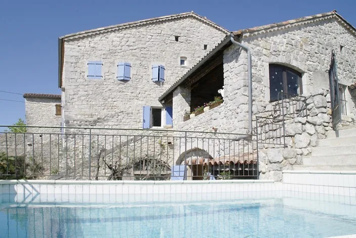 Piscine profonde entourée d'une terrasse avec vue sur le mas en pierre