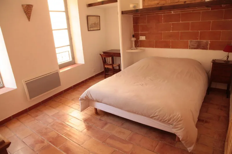 Chambre lumineuse avec lit double, sol en tomettes et mur en pierres apparentes