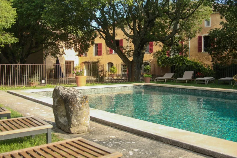 Piscine extérieure sécurisée entourée de transats sous les grands arbres du domaine