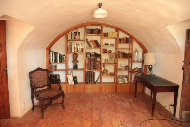 Bibliothèque voûtée avec étagères en bois et fauteuil ancien, espace calme du gîte