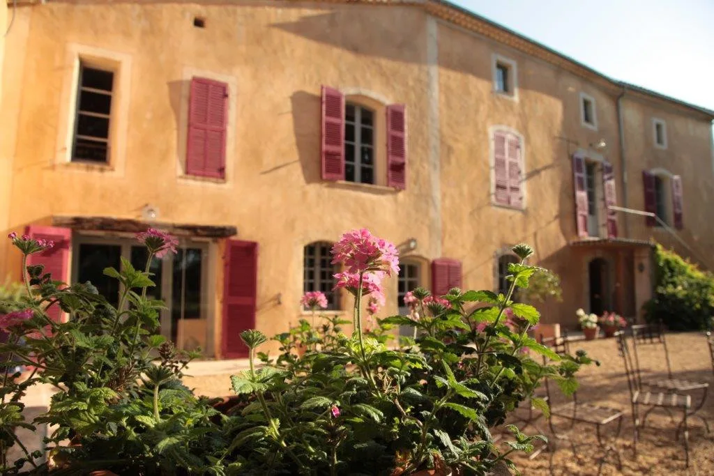 Gîte de groupe Le Gîte du Domaine Gavoty à Cabasse — Façade en pierre du corps de ferme provençal avec volets rouges et massifs fleuris, capacité 15 personnes