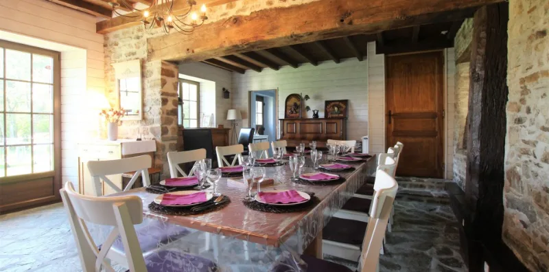 Salle à manger avec poutres apparentes et grande table dressée pour le groupe