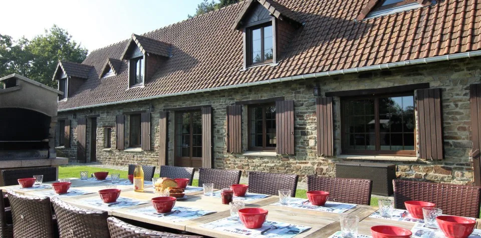 Gîte de groupe Un Coin de Verdure à Souleuvre en Bocage — Façade en pierre du corps de ferme normand avec grande table dressée en terrasse, capacité 14 personnes