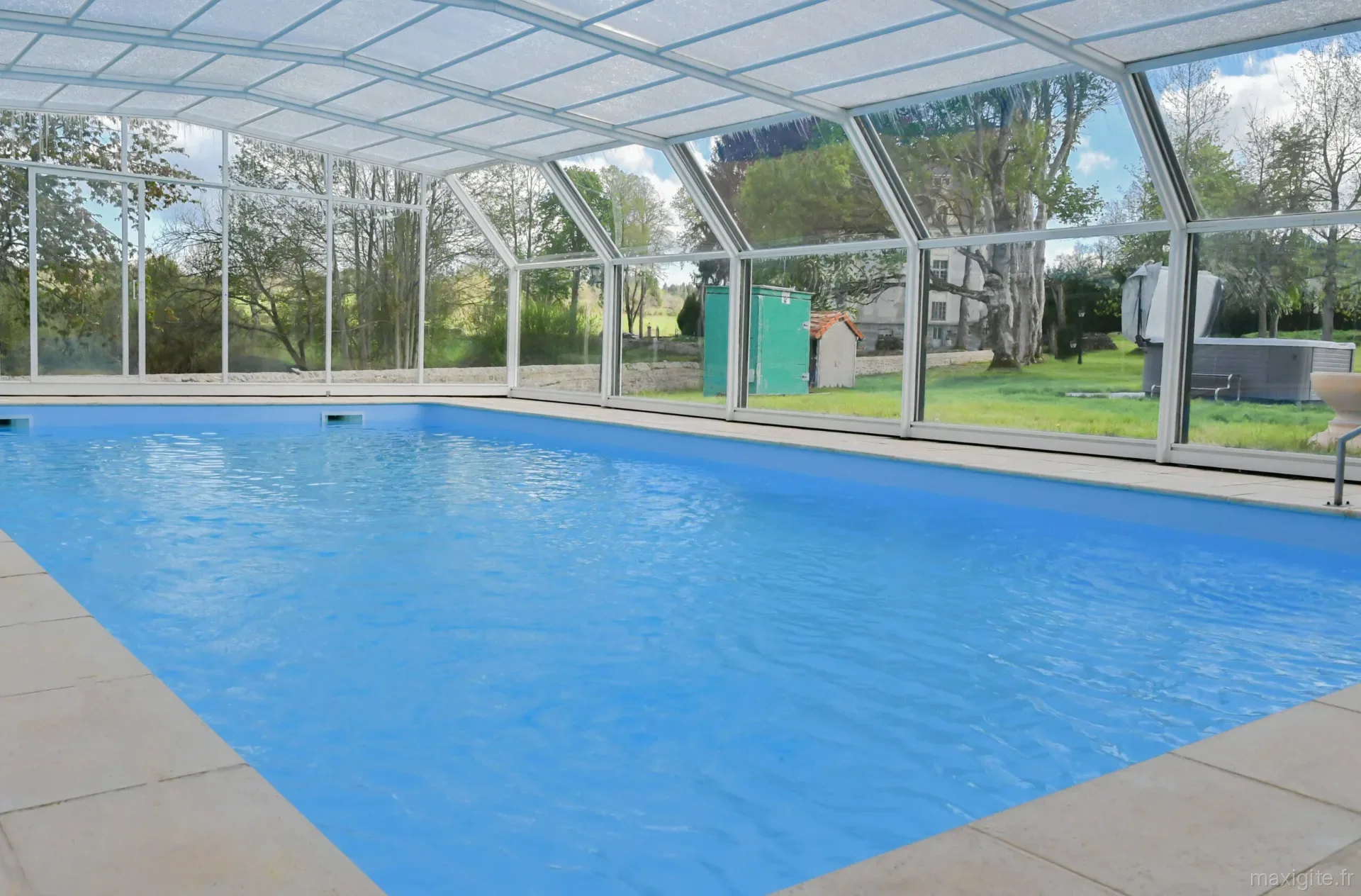 Piscine chauffée sous véranda vitrée avec vue sur le parc arboré et le château