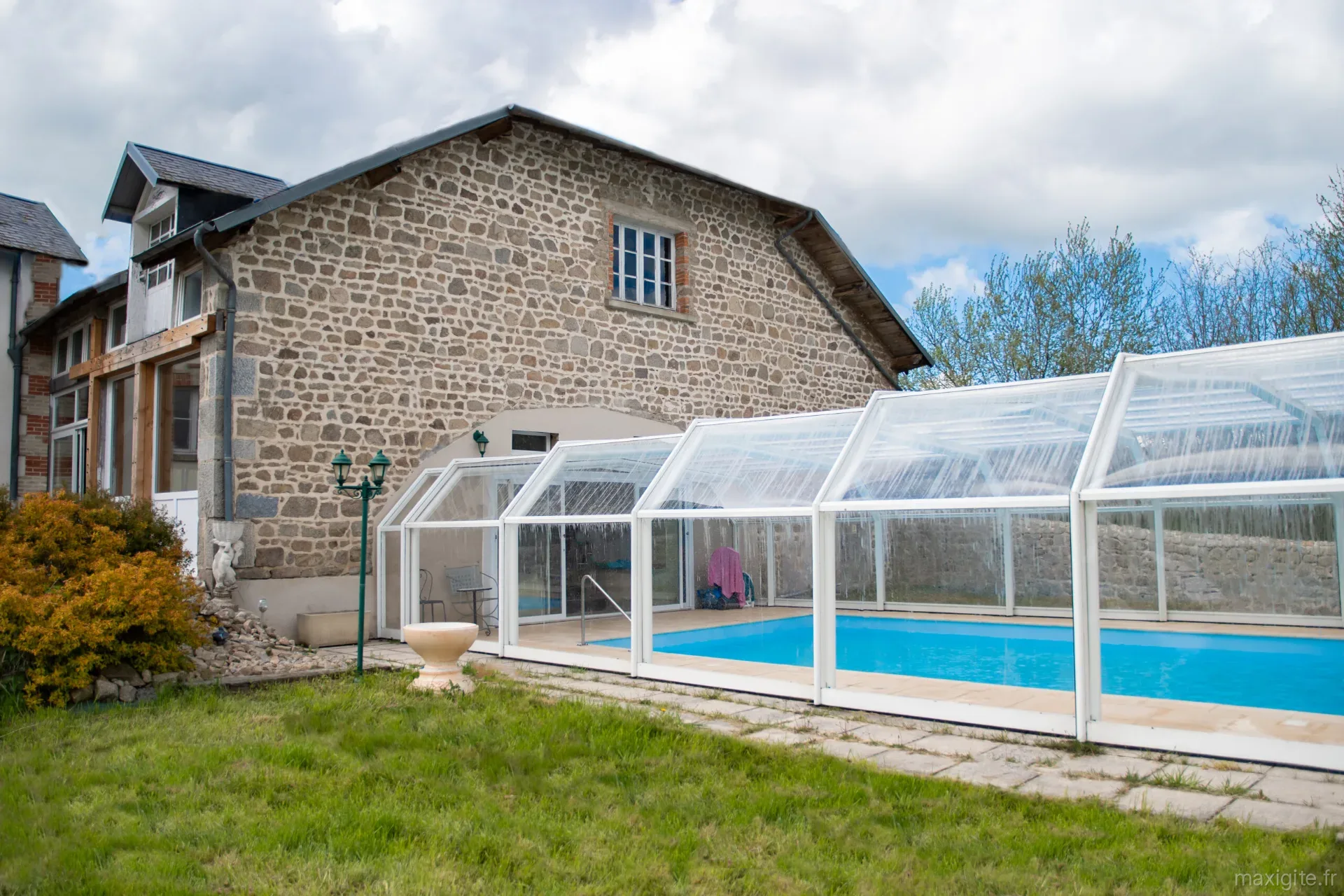 Piscine intérieure couverte avec structure vitrée, transats et vue sur le mur en pierre