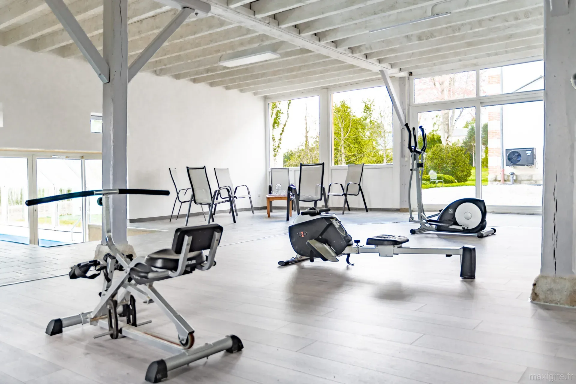 Salle de sport avec vélo elliptique, rameur et appareil de fitness, grandes baies vitrées